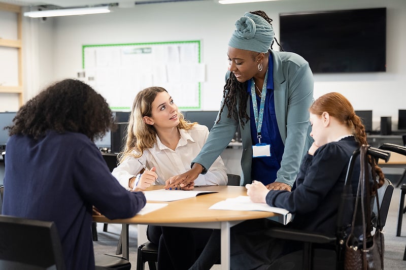 female-students-working-on-assignment-with-help-from-teacher